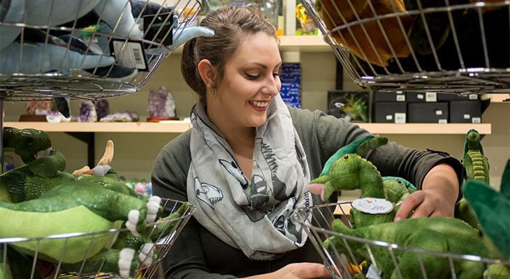 A woman wearing a dinosaur scarf looks at Museum Shop products.