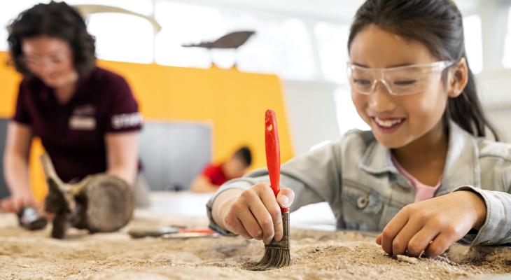 A child uses a paintbrush to remove dirt from a fossil.