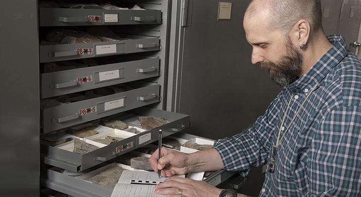 Christopher West looks at fossils in the Museum’s Collections Storage and writes in a notebook. 