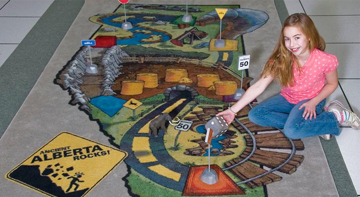 A child rolls a die on a floor-sized game board. 