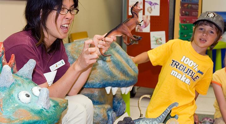 An educator holds a toy dinosaur. 