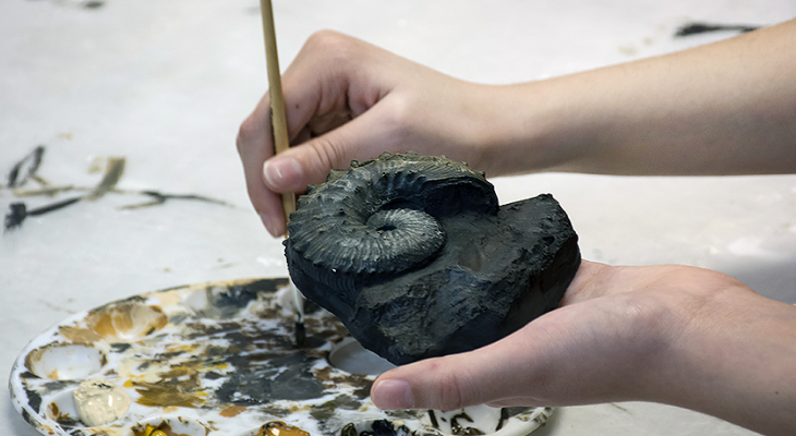 Close-up of a person’s hands painting a cast of a fossil shell.